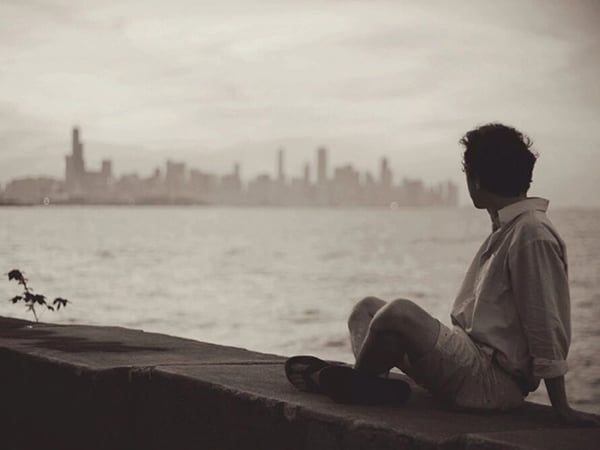 man sitting near body of water looking at city skyline