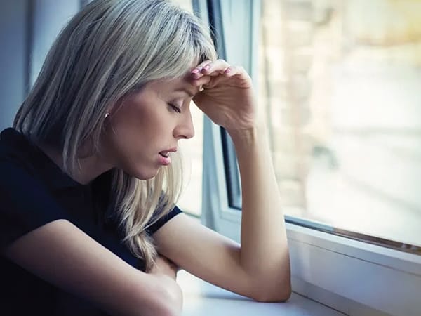 stressed woman with eyes closed with arms resting on windowsill